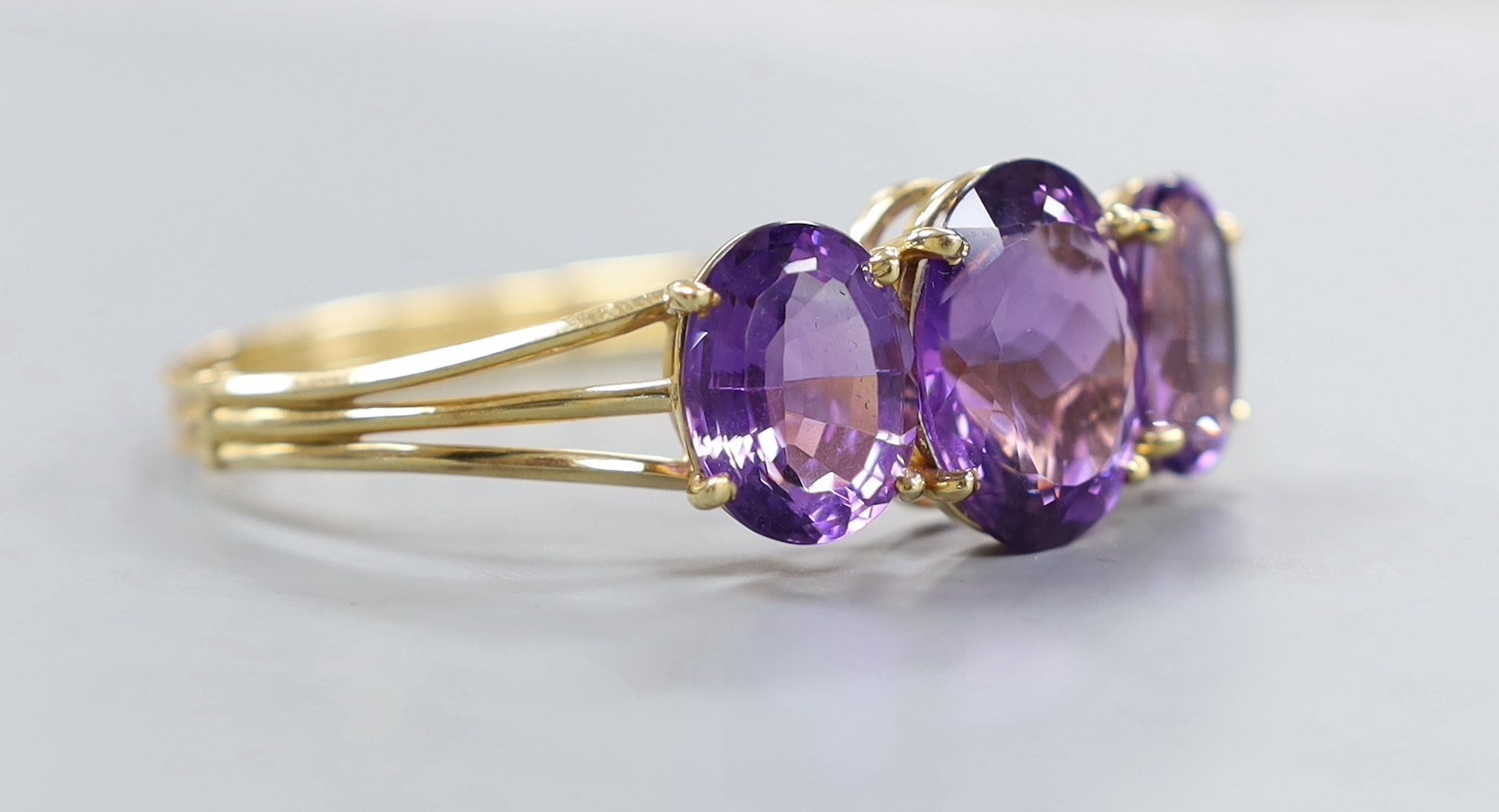 A modern 14k and three stone oval cut amethyst set hinged bangle, interior diameter 54mm, gross weight 24.8 grams.